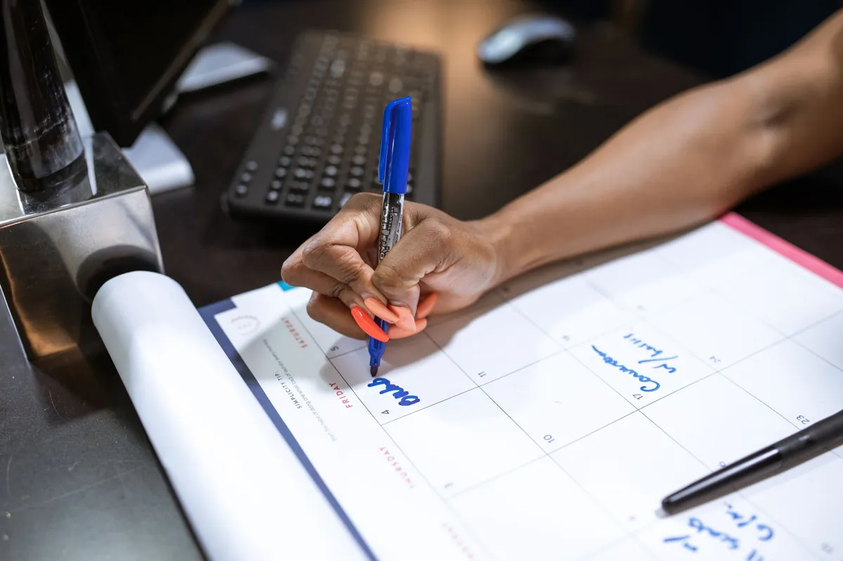 A hand writing notes on a calendar with a blue marker.