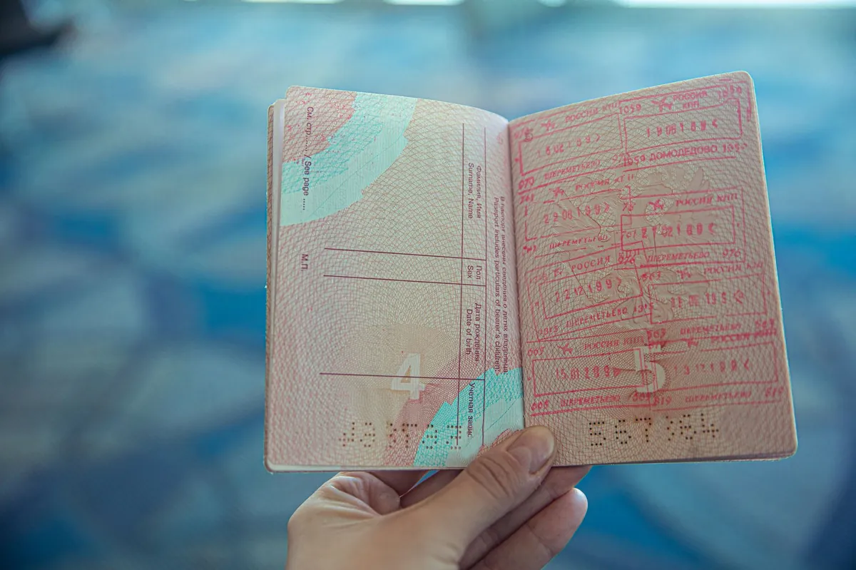 A close-up of an open passport with colorful travel stamps, set against a softly blurred airport background.
